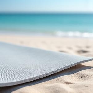 Textured yoga mat designed for sand, partially covered with clean beach sand, next to a seashell.